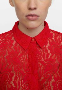 Red lace blouse featuring a collared neck, intricate floral and paisley patterns, and a front button closure.