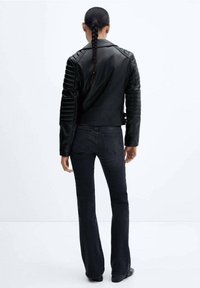 Czarna skórzana kurtka motocyklowa z pikowanymi detalami na ramionach, dopasowanym krojem i krótką długością, w połączeniu z ciemnymi jeansami o prostym kroju.