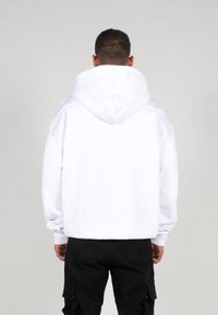 Sudadera blanca con capucha, de corte relajado y mangas largas. Combinada con pantalones cargo negros, el estilo es casual y cómodo.