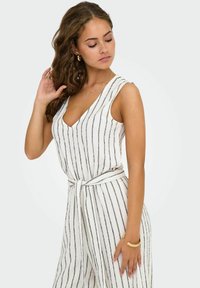 Tuta bianco a righe con linee navy, design senza maniche, scollatura a V profonda, cintura annodata in vita, tessuto strutturato e gambe ampie.