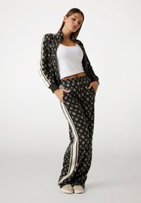 Black tracksuit with white geometric patterns, featuring a zip-up jacket and elastic waist pants, complemented by side stripes and pockets.