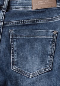 Vaqueros de mezclilla azul oscuro con un solo bolsillo trasero. Costuras prominentes en un tono más claro. Etiqueta de cuero cuadrada en la cinturilla.