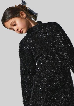 Abito nero a maniche lunghe coperto di paillettes con collo alto. Il materiale testurizzato riflette la luce, creando un effetto scintillante.