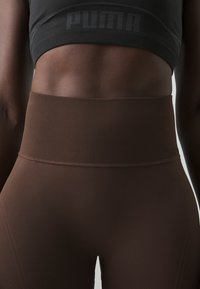 Brązowe legginsy z wysokim stanem z teksturowanym, prążkowanym pasem i gładkim materiałem. Czarna sportowa biustonosz z subtelnym detalem logo.