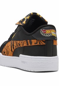Baskets noires et oranges avec un motif rayé de tigre, semelle blanche et logo Hot Wheels Monster Trucks sur l'onglet du talon.