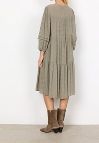 Khaki groene, gelaagde jurk met textuurstrepen, pofmouwen en een knie-lange snit. Gecombineerd met bruin suède enkellaarsjes.