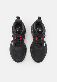 Chaussures de sport noires avec des accents rouges, tige en maille, trois rayures blanches, col rembourré et semelle en caoutchouc texturé.