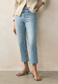 Světlé modré džínové kalhoty s vysokým pasem, s krátkou délkou a neosedlaným lemem. Doplněné černými vzorovanými pantoflemi na podpatku.