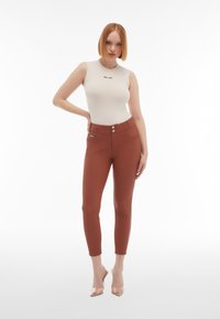 Body ajustado sin mangas de color crema con el texto "día libre", combinado con pantalones de tiro alto en color óxido que cuentan con dos botones y bolsillos delanteros.