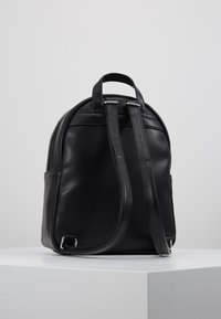 Černý kožený batoh zaobleného tvaru s dvěma držadly nahoře a nastavitelnými popruhy na ramena. Obsahuje stříbrné kovové detaily a strukturovaný povrch.