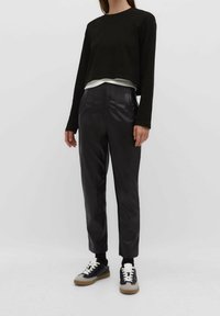 Zwarte cropped top met lange mouwen, gelaagd over een wit shirt. Hooggetailleerde, geplooide zwarte broek, gecombineerd met zwart en beige sneakers.