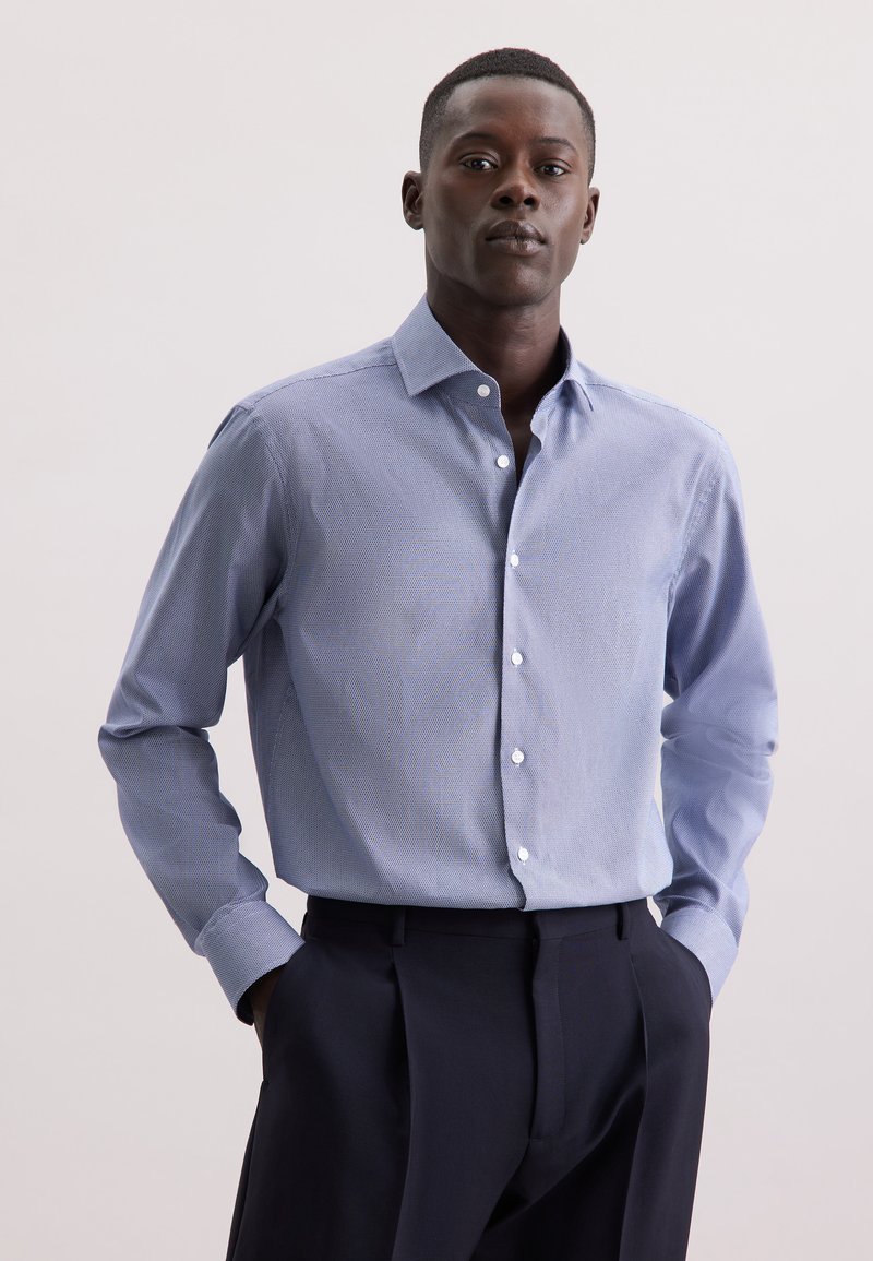 Camicia azzurra chiara con un motivo sottile, maniche lunghe e colletto. Abbinata a pantaloni scuri, che mostrano una vestibilità su misura.