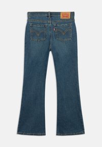Jeans flared de denim azul com cintura alta, apresentando dois bolsos traseiros e costura amarela contrastante, exibindo um leve efeito vintage.