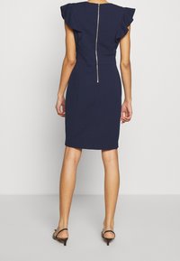 Robe ajustée bleu marine avec de courtes manches volantées, une fermeture éclair dissimulée dans le dos et une longueur au genou. Texture lisse avec un léger stretch.