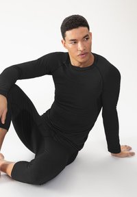 Schwarzes eng anliegendes Langarmoberteil mit rundem Halsausschnitt und Raglanärmeln, kombiniert mit schwarzen kurz geschnittenen, eng anliegenden Leggings. Glatte Textur, minimalistisches Design.