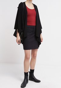 Schwarze, offen getragen Cardigan, rotes, enges Tanktop, schwarzer Bleistiftrock, schwarze Stiefeletten, mit einem einfachen, eleganten Design. Textilstruktur, moderner Look.