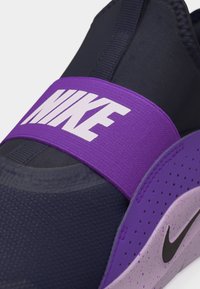Gros plan sur une chaussure Nike noire et violette avec une large bride violette ornée du texte blanc Nike sur le dessus.