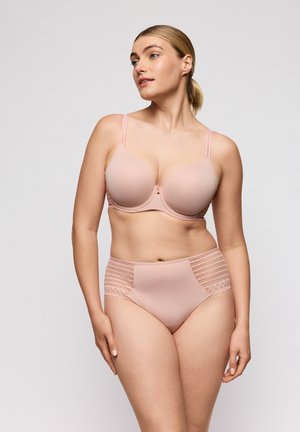 Vrouw die een lichtroze beha en bijpassende hoge slipjes met kanten rand draagt, kijkt iets naar links tegen een effen achtergrond.