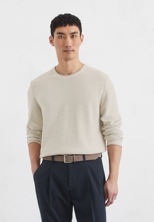 Beige, textuurtrui met lange mouwen en een ronde halslijn, gecombineerd met marineblauwe broek en een lichtbruine riem. Neutrale kleurenpalet.