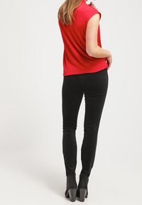 Top rojo sin mangas combinado con pantalones negros ajustados. El conjunto presenta una tela suave y un diseño entallado, con botas de tacón alto.