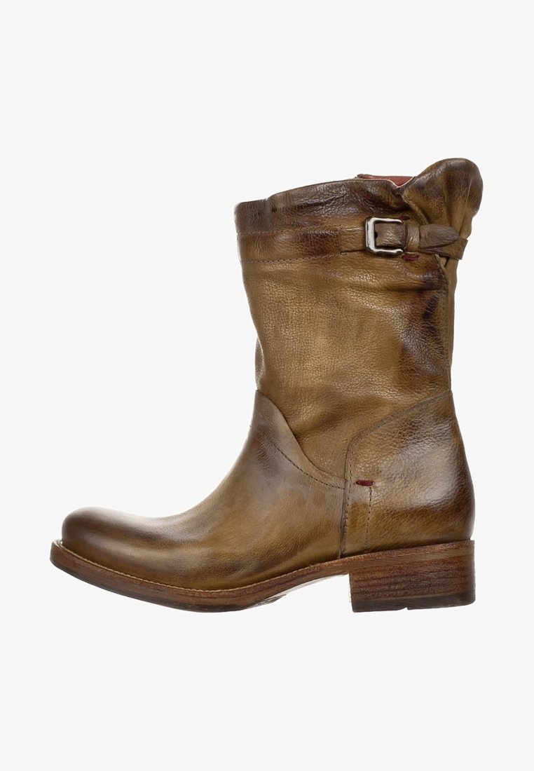 Ruskea nahkainen nilkkuri löysällä muotoilulla, solkiyksityiskohdalla, pyöreällä kärjellä ja pinotulla puisella korolla; teksturoitu pinta, jossa hienovarainen kulunut ilme.