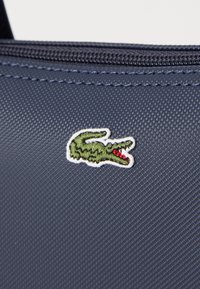 Navy textured fabric featuring a green crocodile logo with red accents, embroidered on a smooth surface with a zipper closure.