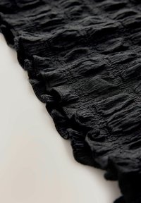 Zwarte textuur stof met een golvend patroon en gerolde randen. Het materiaal lijkt lichtgewicht en iets doorschijnend.