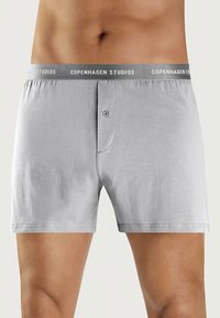 Grå boksershorts med en blød bomuldsstruktur, der har en knaplukning og et kontrastfarvet elastisk bælte med "Copenhagen Studios" branding.