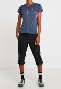 Camiseta atlética de color azul marino con detalles en rosa, de mangas cortas y con cremallera frontal. Pantalones cortos negros hasta la rodilla y zapatillas negras con detalles en aqua.