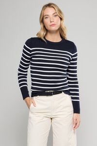 Maglione a righe blu navy e bianche con scollo rotondo e maniche lunghe, con bottoni decorativi sulla spalla. Indossato con pantaloni beige.