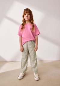 T-shirt rose en coton avec logo, associé à un pantalon ample à motif floral vert et des baskets blanches. Textiles lisses, coupe décontractée.
