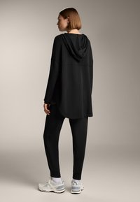 Felpa nera con cappuccio e vestibilità comoda, abbinata a pantaloni jogger neri a gamba affusolata e sneaker grigie. Tessuto liscio, design semplice.