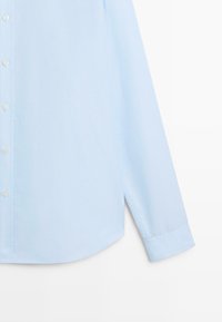 Svetle modrá košile na knoflíky s dlouhými rukávy, zaobleným lemem a jemnou texturou látky. Obsahuje klasický límec a šest předních knoflíků.