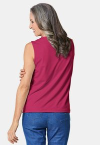 Mouwloze top van levendig roze stof, met een gladde textuur en eenvoudig ontwerp. Gepaard met blauwe spijkerbroek, bekeken vanuit de achterkant.