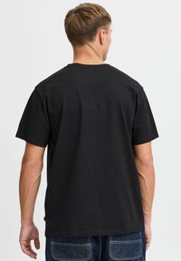 Camiseta de algodón negra de manga corta, con cuello redondo y un corte relajado. Diseño sencillo sin logotipos ni patrones visibles en la parte posterior.
