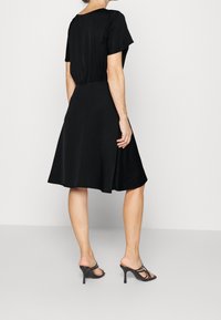 Černé šaty s krátkými rukávy, přiléhavým živůtkem a rozšířenou sukní. Hladká látka s mírným leskem. Nositelná s černými sandály na podpatku.