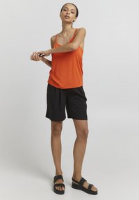 Orange ærmeløs top, blødt stof, med tynde stropper; parret med sorte shorts, glat tekstur, knælange; båret med sorte sandaler.