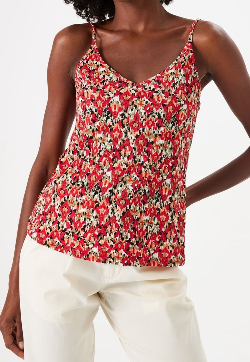 Camisole rouge et blanche à motifs avec de fines bretelles, ornée d'un motif floral et d'une texture froncée. Portée avec un pantalon de couleur claire.