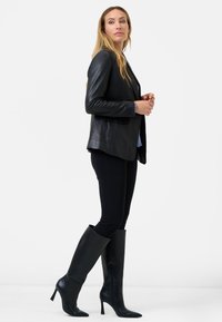 Black leather blazer with a tailored cut, paired with fitted black leggings and knee-high stiletto boots. Smooth texture and sleek design.