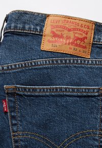 Poche arrière d'un jean en denim avec étiquette en cuir Levi Strauss indiquant la taille W32 L32 et étiquette en tissu rouge Levi's sur la couture latérale.