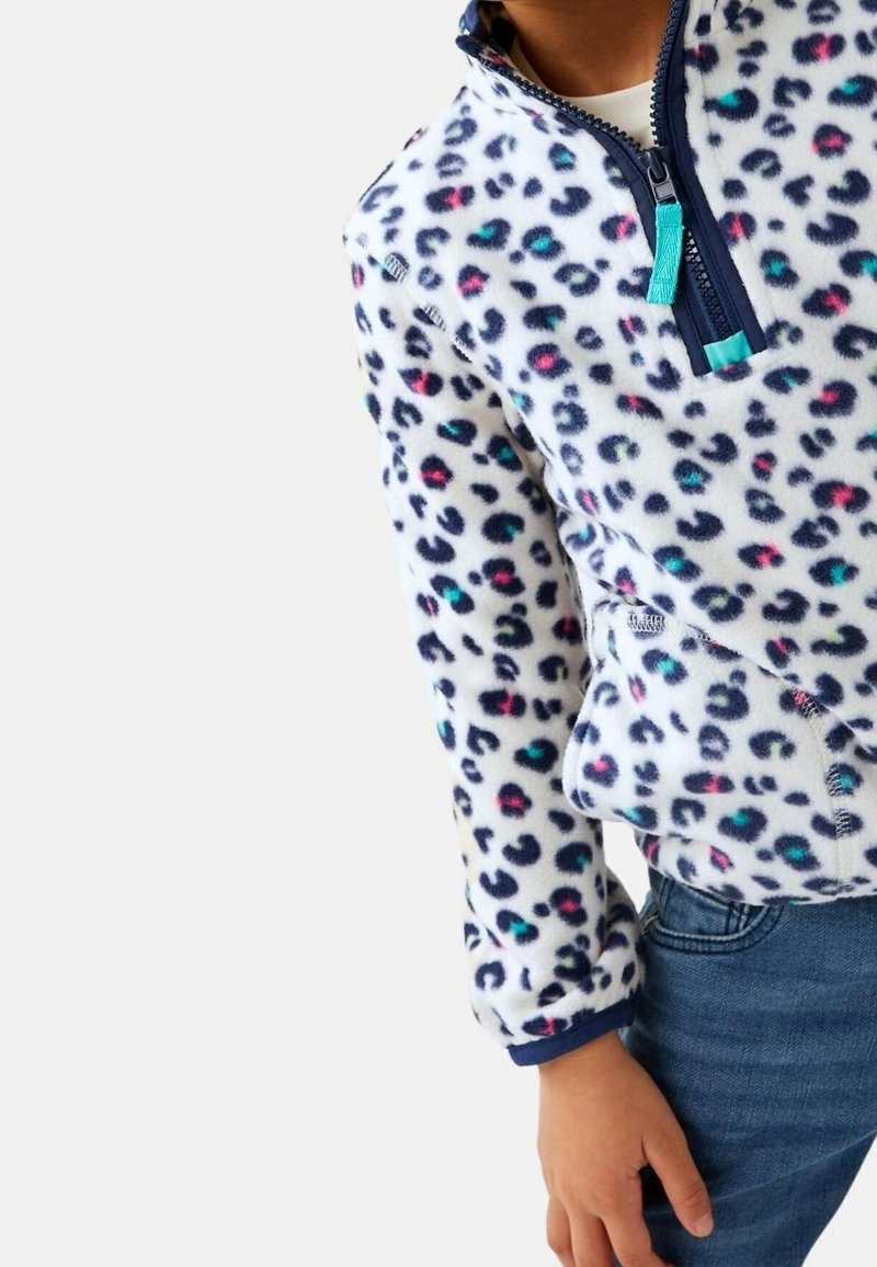 Enfant portant un pull polaire blanc avec une fermeture éclair quart, orné d'un imprimé léopard coloré, associé à un jean bleu.