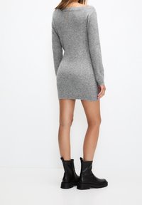 Robe pull grise en maille avec manches longues, coupe ajustée et encolure bateau, associée à des bottines noires à semelle épaisse.