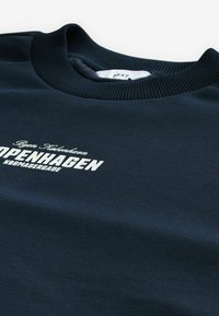 Námornícky modrý sweatshirt s rebrovaným výstrihom, s nápisom "COPENHAGEN" v bielej farbe. Mäkká látka s hladkou textúrou a minimalistickým dizajnom.
