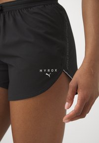 Black athletic shorts made of lightweight material, featuring a textured fabric, side slit, and printed logos "HYROX" and Puma.