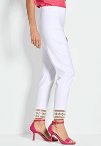 Witte broeken met een gladde textuur, voorzien van een decoratieve kanten rand aan de zoom. Gecombineerd met roze hoge hakken sandalen.