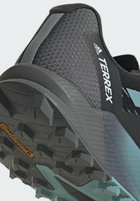 Scarpa atletica nera con tomaia in rete texturizzata, dotata di un accento blu e una suola robusta con grip multidirezionale contrassegnata "Continental."