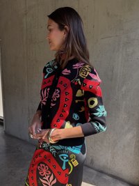 Pletený kardigán s multicolor grafickým vzorom, prevažne červený, čierny a teal. Dlhé rukávy a priliehavý strih.