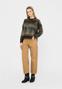 Bieza adīta džemperis tumšās toņos ar pakāpenisku rakstu, kombinēts ar bēšām darba biksēm; modelis valkā melnus potīšu zābakus ar kniedētām detaļām.