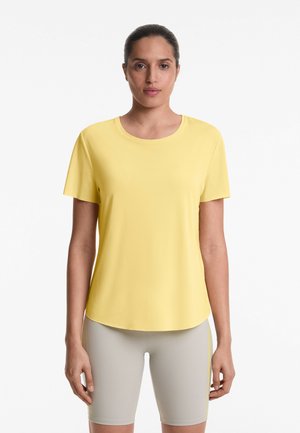 T-shirt gialla a maniche corte con scollo arrotondato e dettagli a pannelli perforati, abbinata a pantaloni shorts grigi chiari da ciclista con strisce laterali.