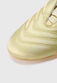 Topánka s lesklým svetlozeleným zvrškom, zdobená prešívanými vlnkovými vzormi a zaoblenou špičkou. Svetlé šnúrky a podrážka v farbe gumy.